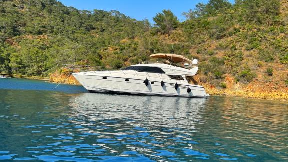 Motor yacht Hadron is anchored in a bay surrounded by green forests.